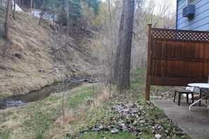 Un patio trasero con cerco de madera, un pequeño arroyo y una mesa de picnic.