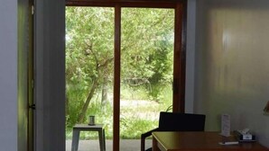 Une pièce dotée d’une porte-fenêtre coulissante donnant sur un jardin, d’une petite table avec une chaise, et d’une table en bois avec une chaise.