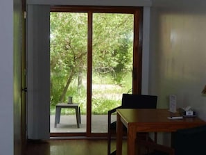 A room with a sliding glass door leading to a garden, a small table with a chair, and a wooden table with a chair.