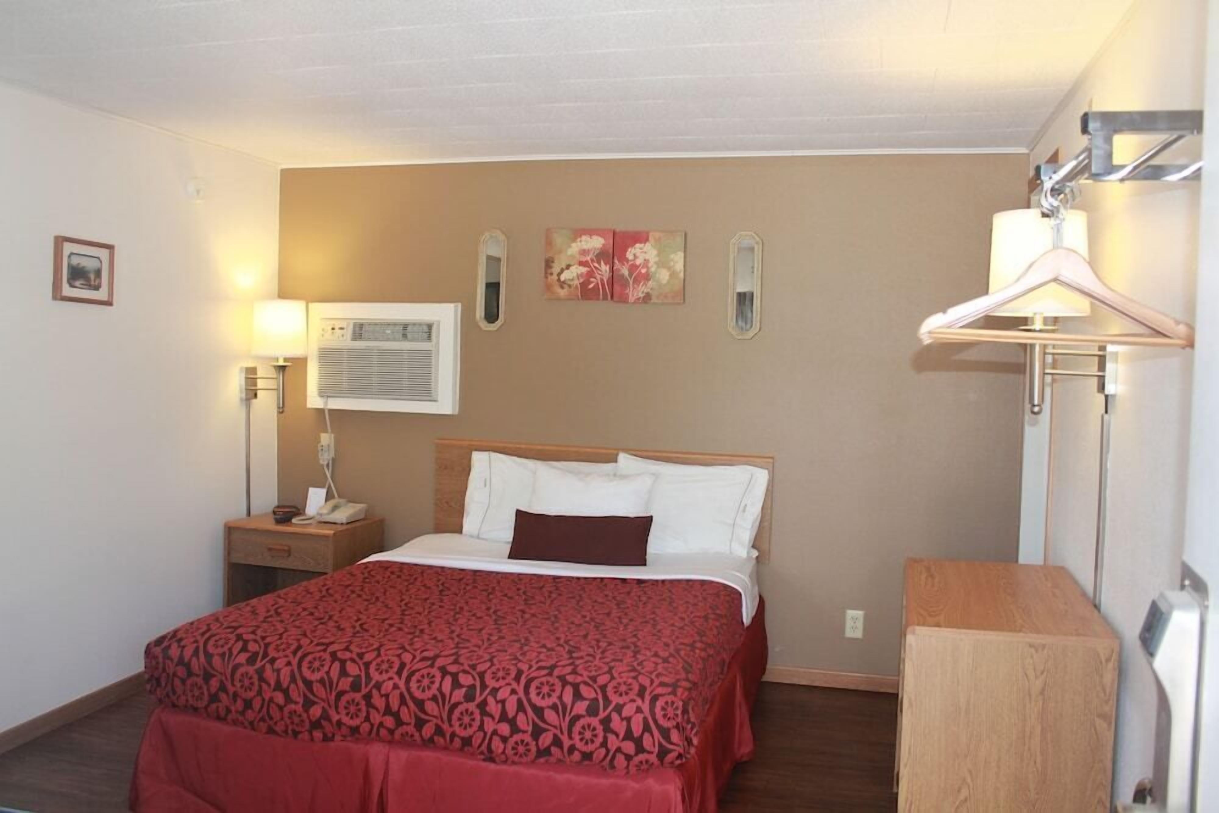 Una habitación de hotel con cama, lámpara de noche, equipo de aire acondicionado y mesita de madera.