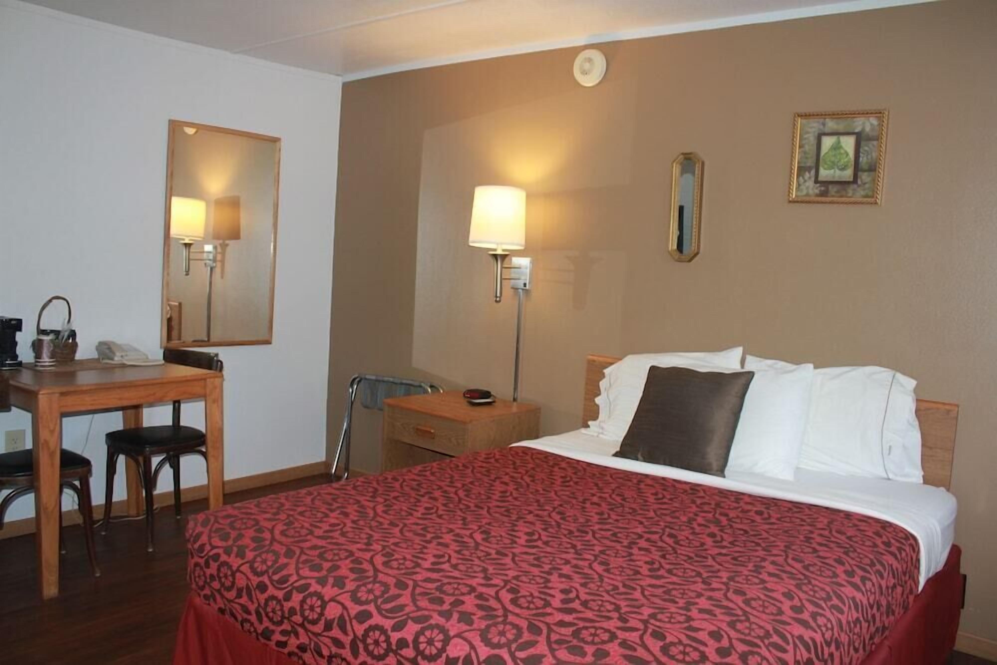 A hotel room with a bed, a desk with a chair, a lamp, and a mirror.
