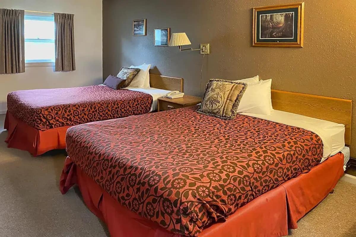 Habitación de hotel con dos camas, cada una con una colcha estampada, una mesita de noche, una lámpara y cuadros en la pared.