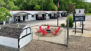 Un motel doté d’un espace extérieur aménagé avec des sièges et délimité par une clôture, d’un foyer et d’une enseigne indiquant qu’il s’agit du Brookside Motel.