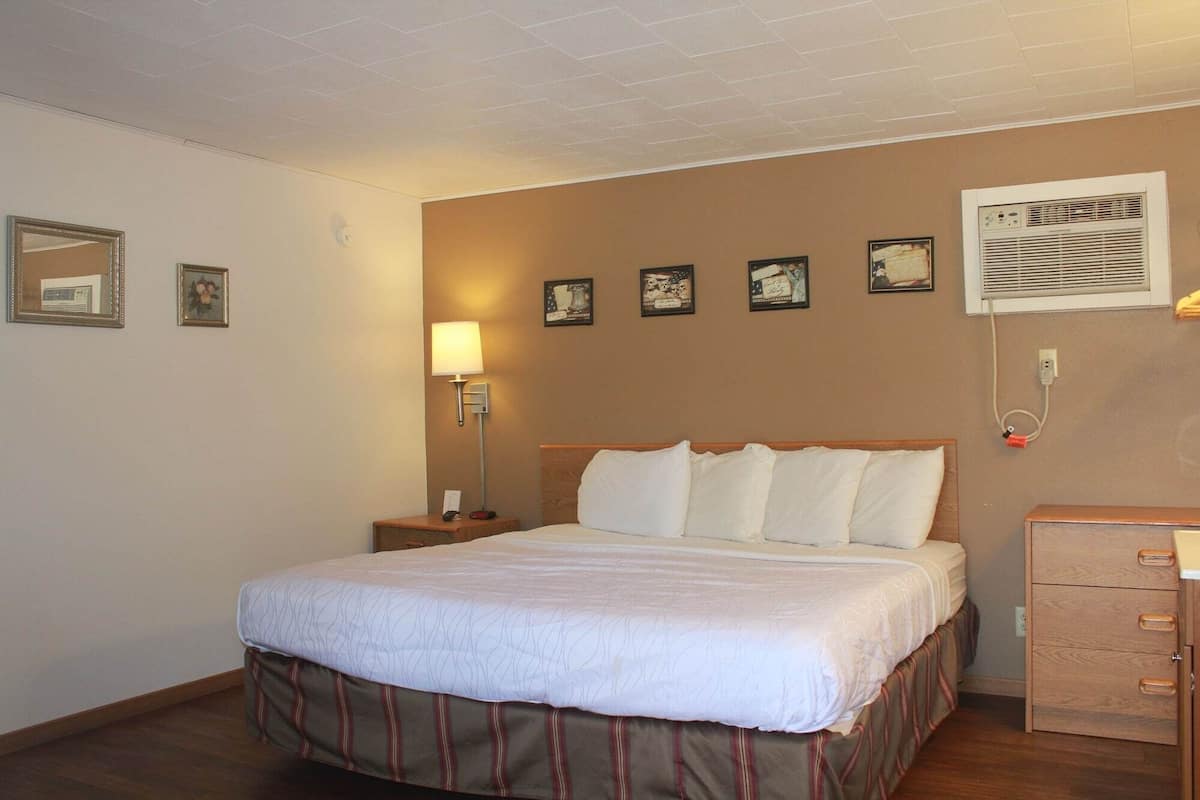 Habitación de hotel con cama, lámpara de noche, aire acondicionado instalado en la pared y cómoda de madera.