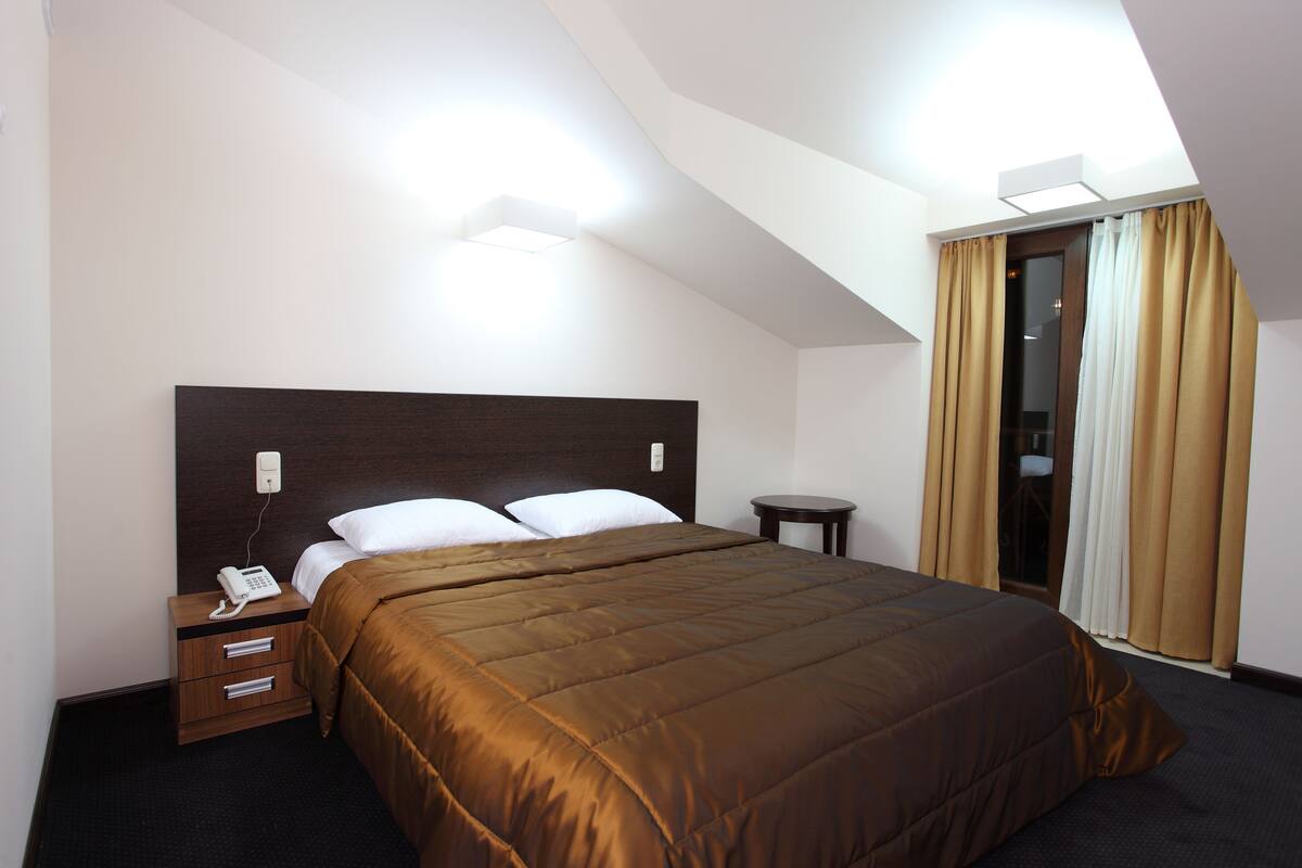 Habitación de hotel con una cama grande, una mesita de noche con teléfono y una ventana con cortinas.