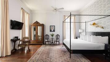 Une chambre d’hôtel avec un lit à baldaquin, un grand miroir, une télévision, une petite table avec des chaises et un tapis à motifs.
