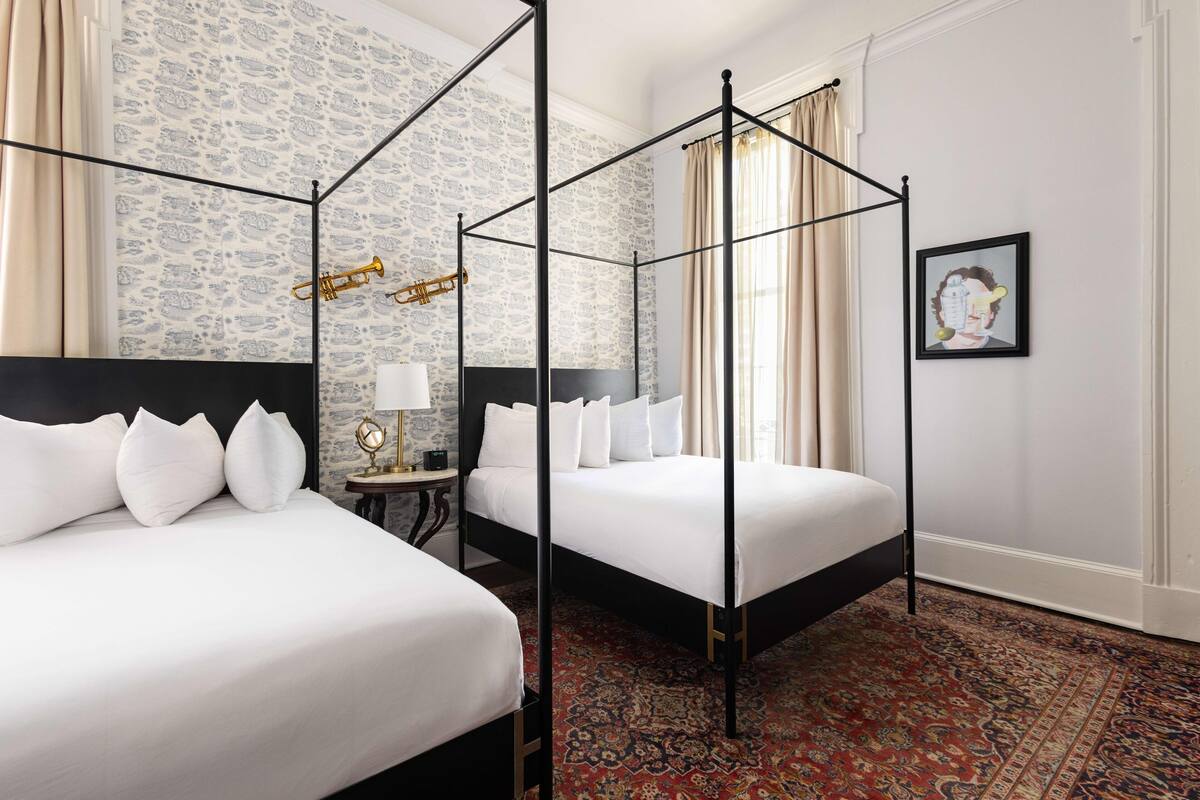 A hotel room with two beds, a four-poster canopy, a patterned carpet, and a framed picture on the wall.