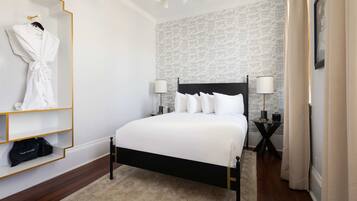 A neatly arranged hotel room with a bed, bedside lamps, a robe, and a shelf with a bag.