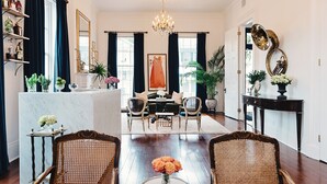 A spacious living room with a dining area, featuring a chandelier, wicker furniture, and a large mirror. - Henry Howard Hotel (New Orleans)