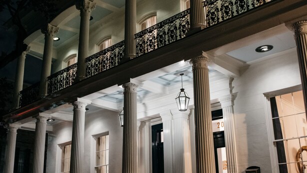 A building with large columns, a balcony with ornate railings, and a well-lit entrance. - Henry Howard Hotel (New Orleans)
