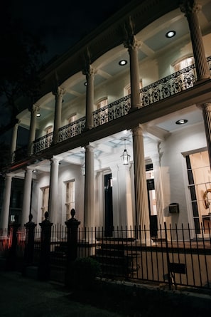 A building with large columns, a balcony with ornate railings, and a well-lit entrance. - Henry Howard Hotel (New Orleans)