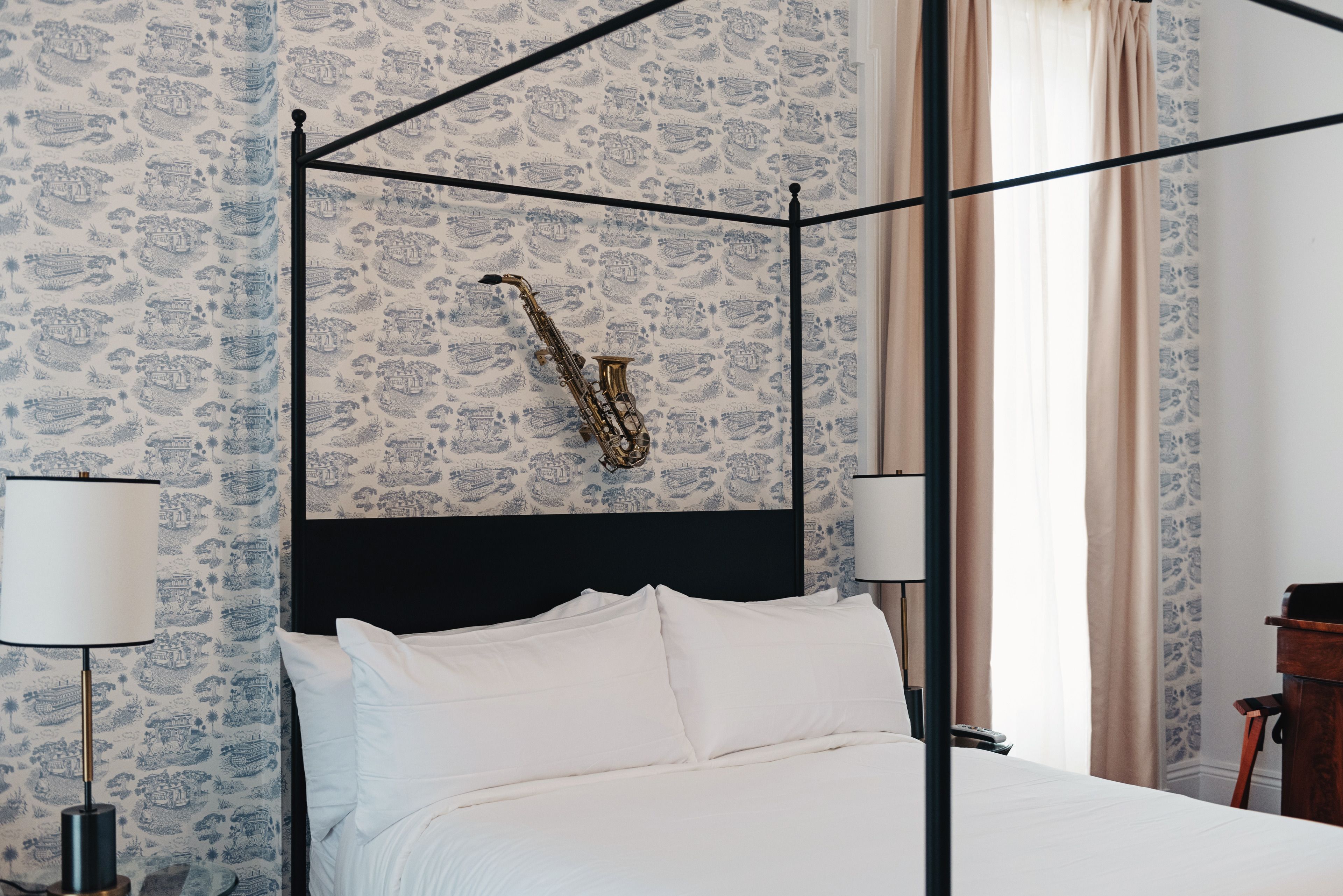 A four-poster bed with white linens, a dark headboard, and a saxophone hanging on the wall.