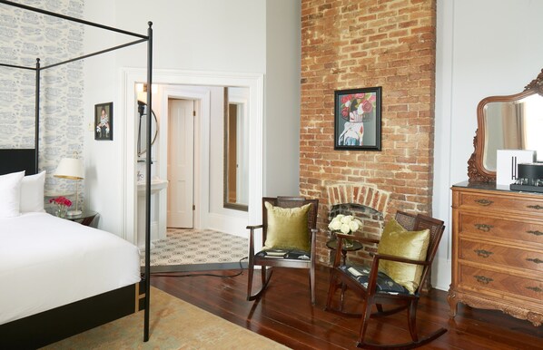 A bedroom with a four-poster bed, a brick wall, a fireplace, and a wooden dresser. - Henry Howard Hotel (New Orleans)