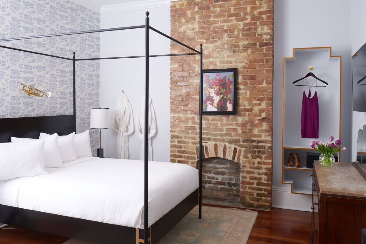 A modern bedroom with a four-poster bed, a brick fireplace, and a mirror with a wooden frame.