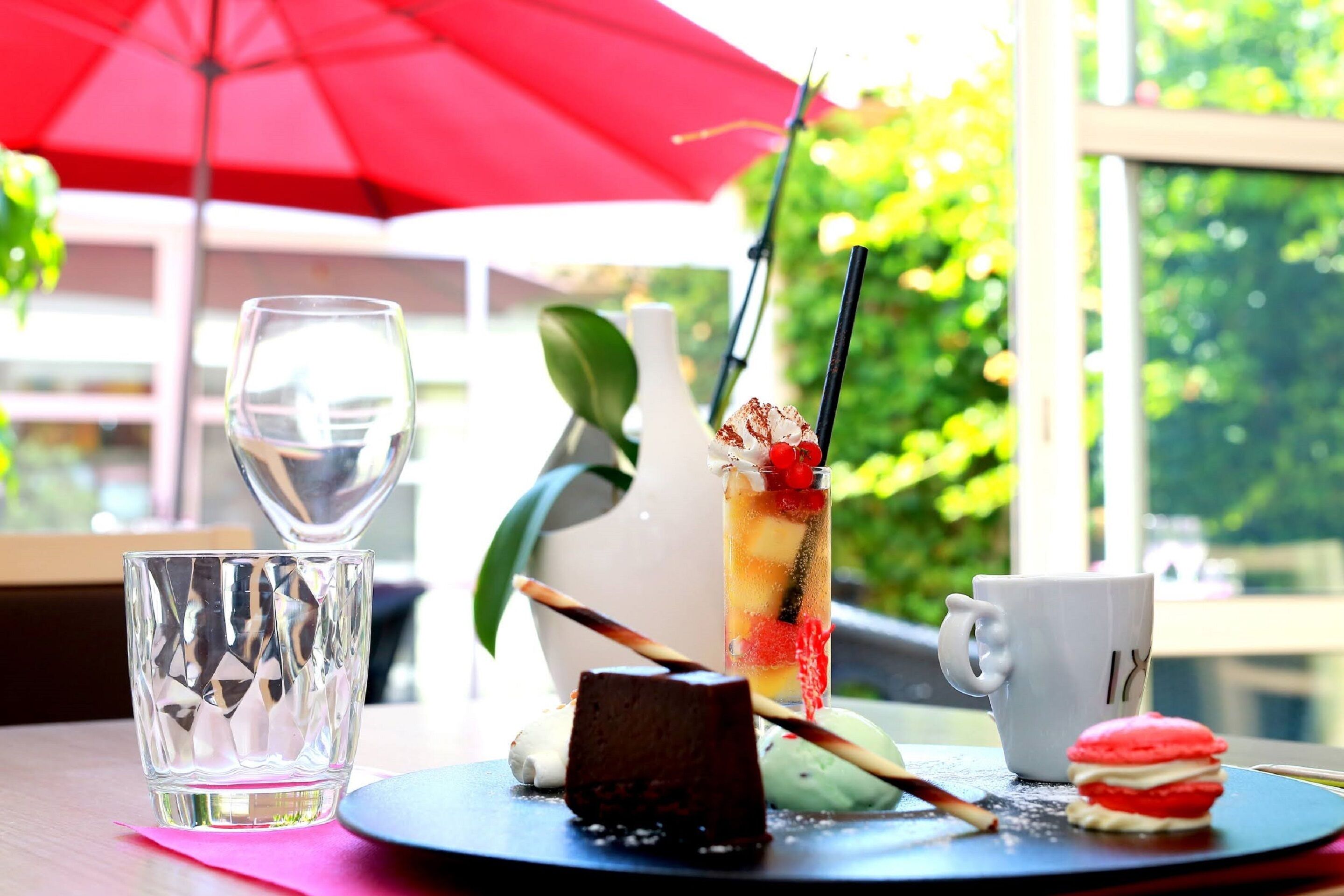 Une table avec une assiette à dessert, un verre d’eau, un grand verre contenant une boisson aux fruits et une paille, et une tasse blanche.