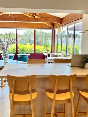A modern dining area with a large table, wooden chairs, and large windows offering a view of greenery.