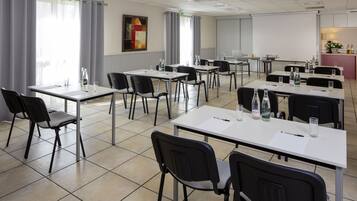 A conference room with multiple tables and chairs, a projector screen, and a kitchenette area.