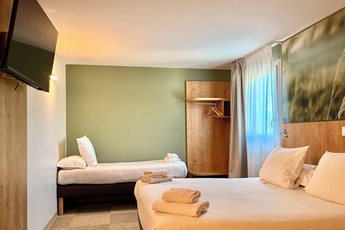 Une chambre d’hôtel avec deux lits, une armoire en bois, un téléviseur à écran plat et une grande fenêtre avec des rideaux.