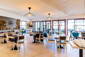 A spacious restaurant with high ceilings, modern pendant lighting, and large windows offering natural light.