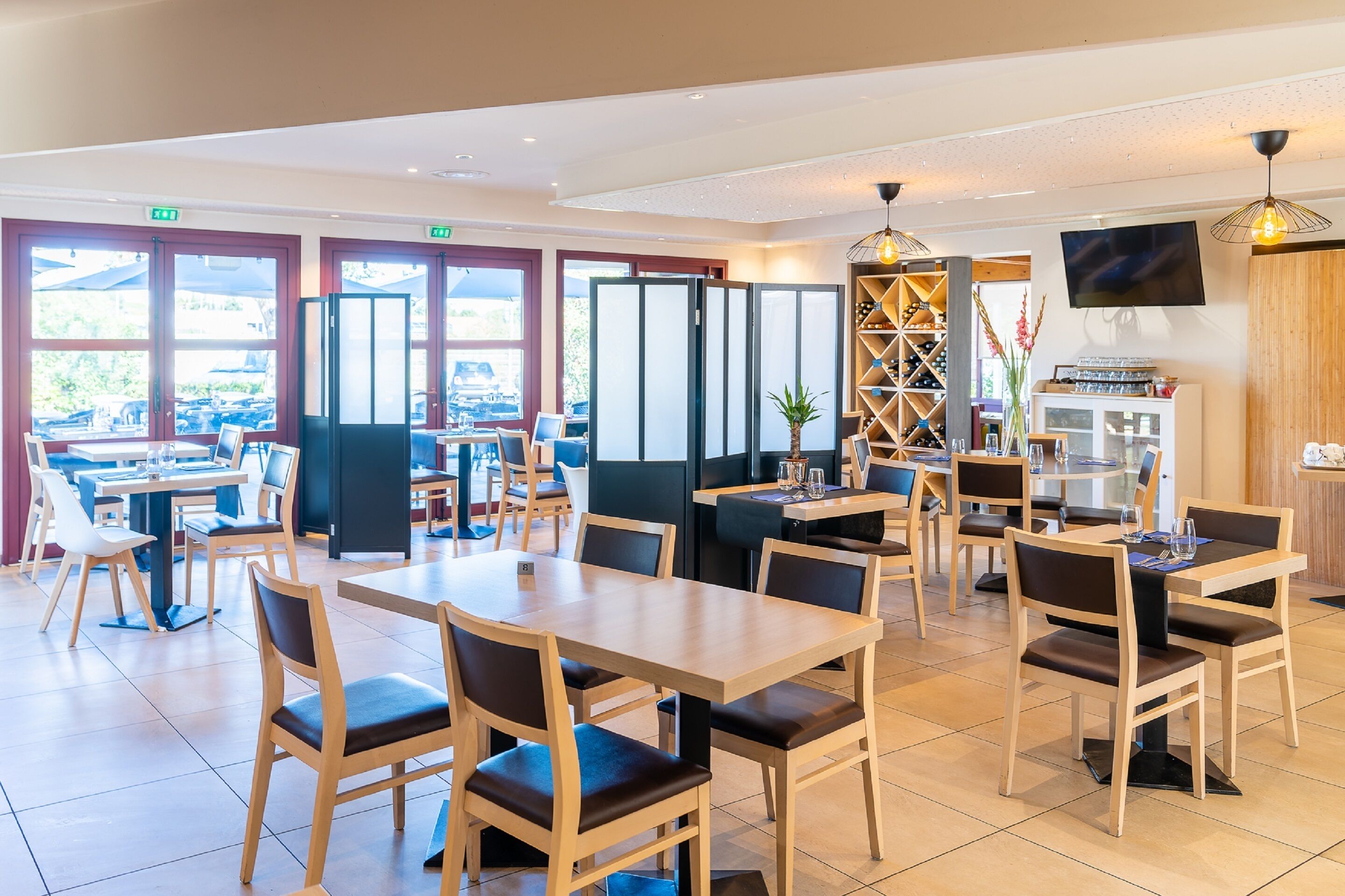 Ein modernes Restaurant mit Holztischen und -stühlen, großen Fenstern und einem an der Wand befestigten Fernseher.