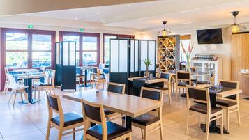Ein modernes Restaurant mit Holztischen und -stühlen, großen Fenstern und einem an der Wand befestigten Fernseher.