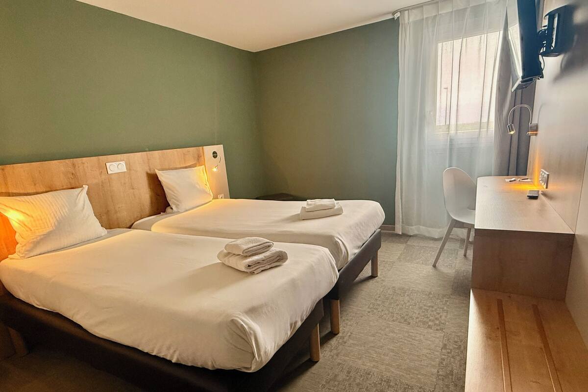 Une chambre d’hôtel avec deux lits, un bureau et une chaise.