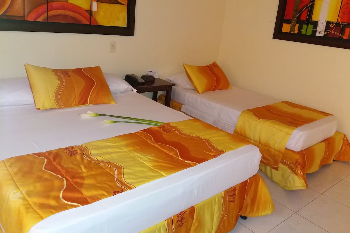 A hotel room with two beds, each with orange and white bedding, a small bedside table with a phone and a lamp, and a painting on the wall.