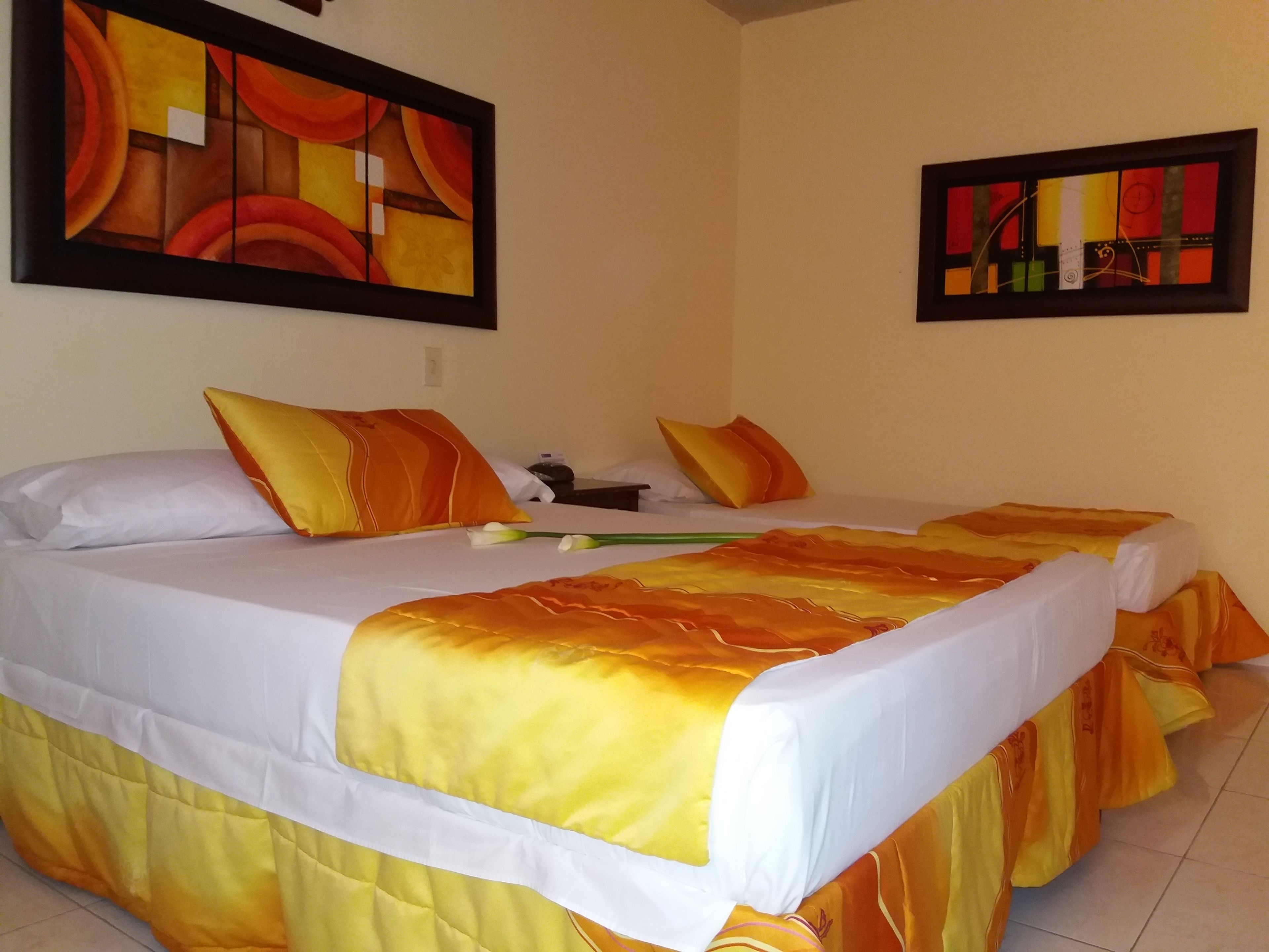A hotel room with two beds, each with orange and white bedding, and two paintings on the walls.