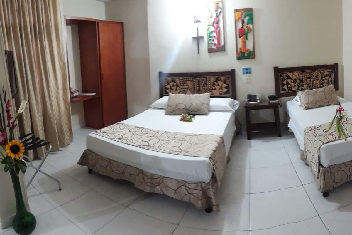 A hotel room with two beds, a wooden wardrobe, a small table, and a vase with flowers.