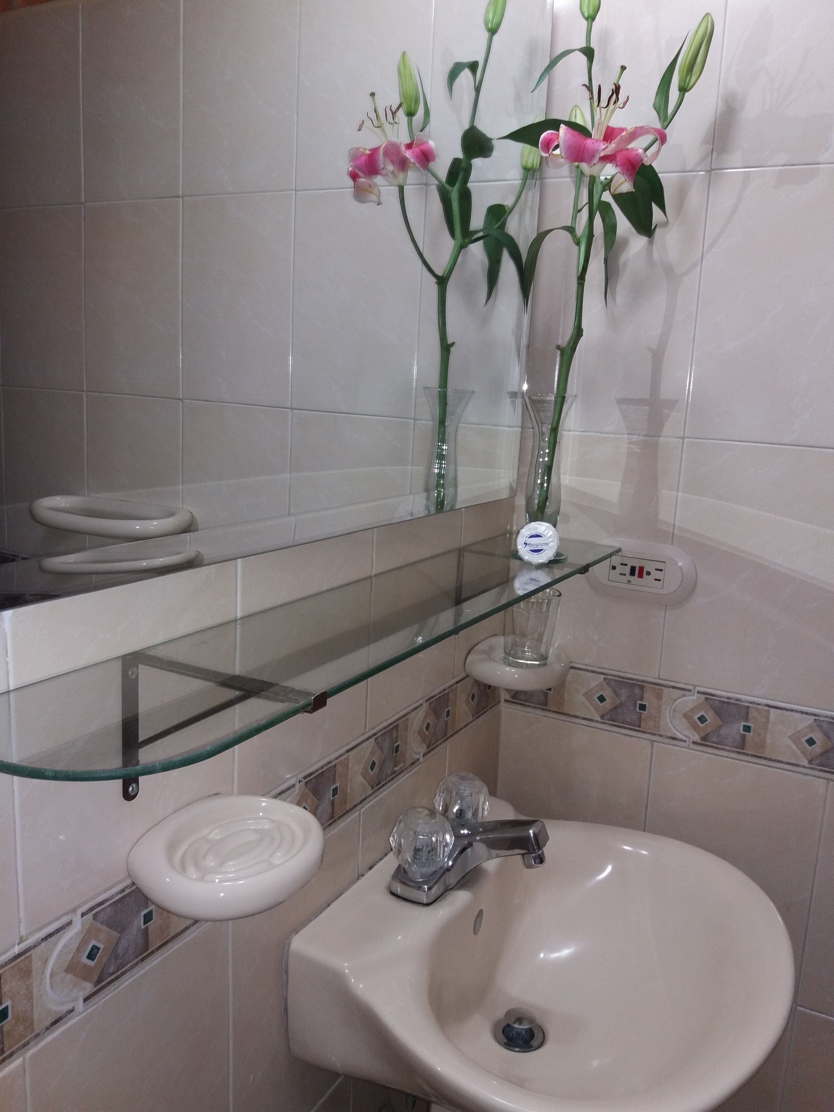 A bathroom with a glass shelf, a sink, and a mirror.