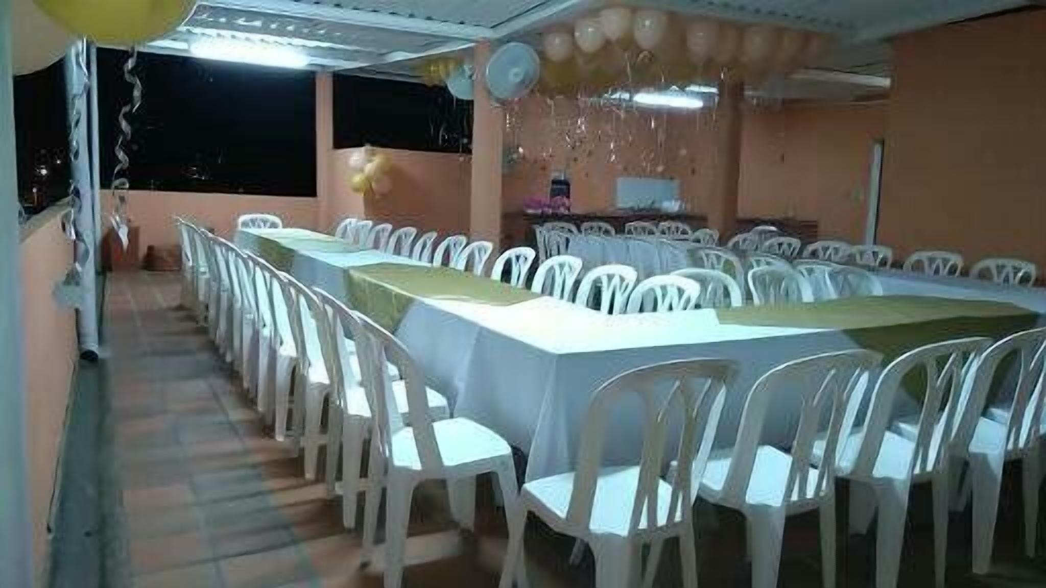 A banquet hall with long tables and white chairs, a stage with a podium, and balloons.