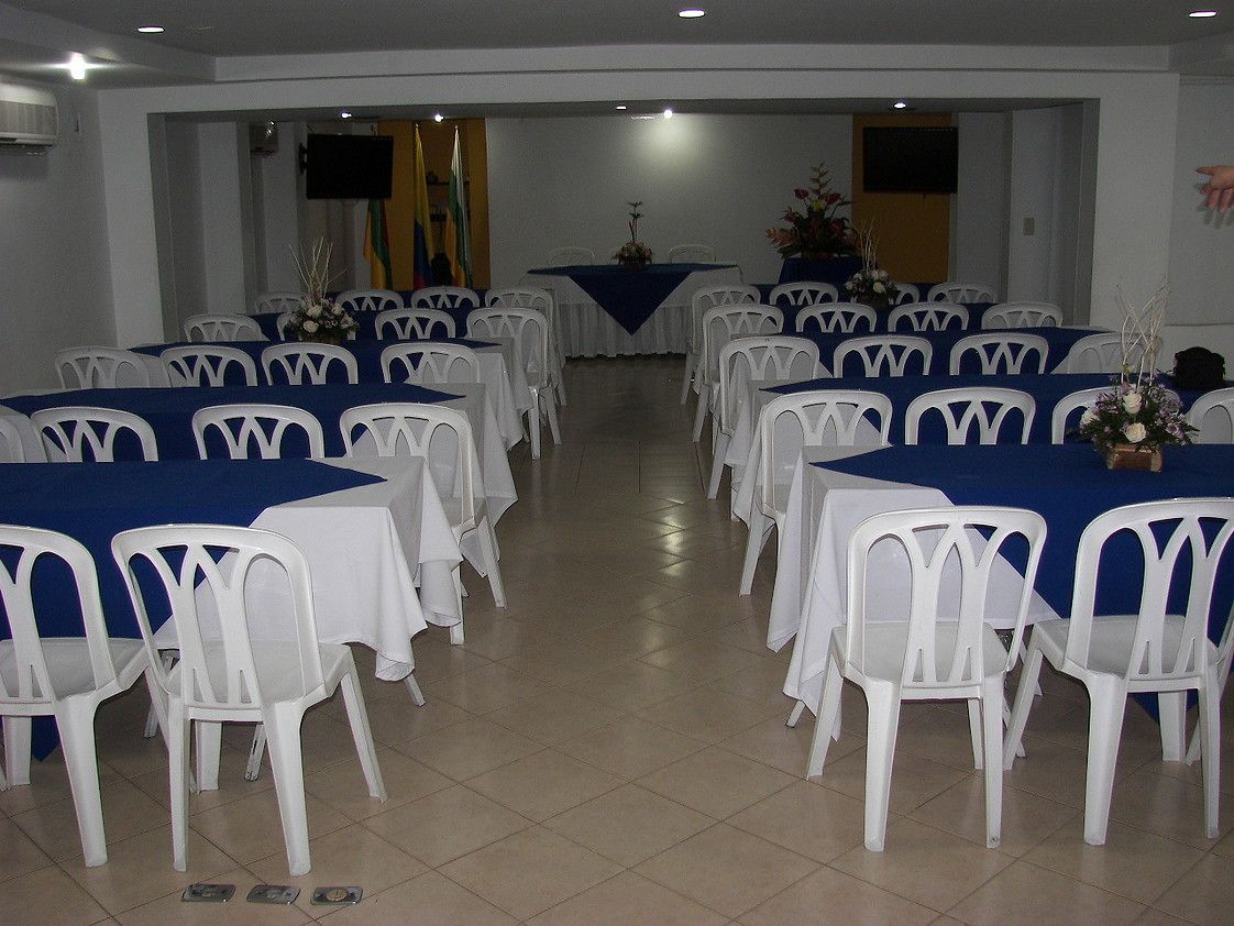 A conference room with rows of white plastic chairs and tables, each covered with a blue tablecloth.