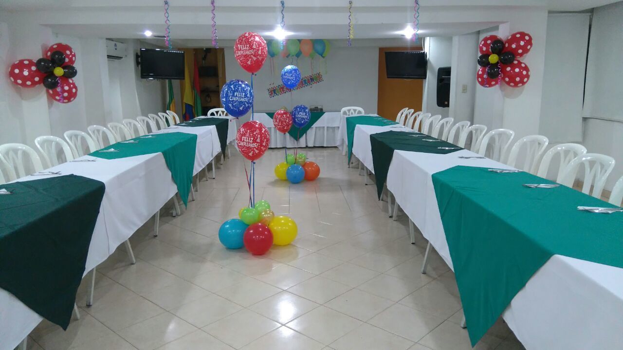 Un salón de conferencias con sillas y mesas blancas, globos y decoraciones florales en las paredes.