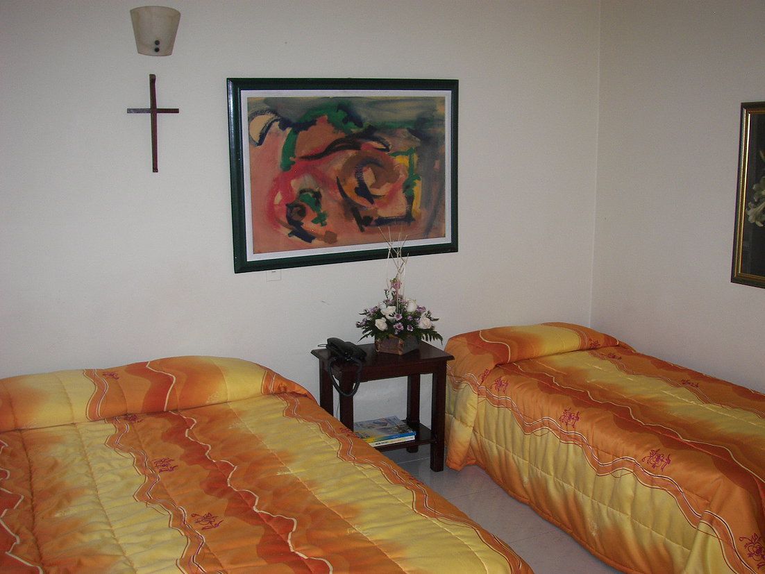 Una habitación con dos camas, una cruz en la pared y un cuadro enmarcado.