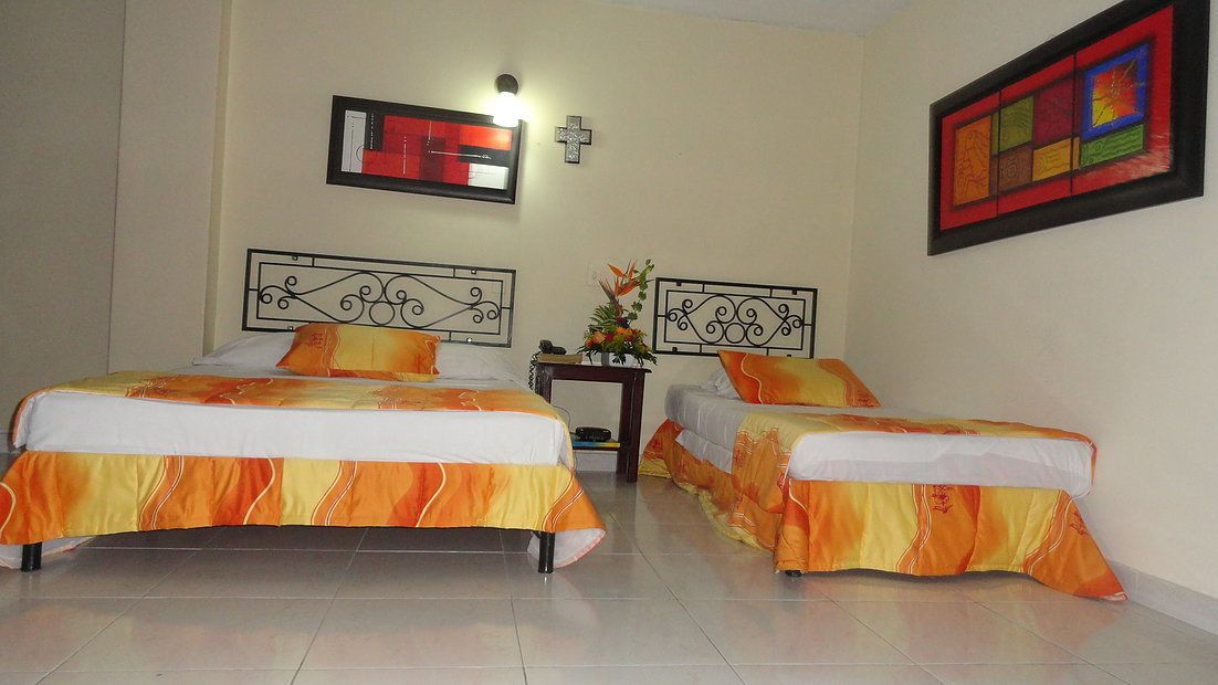 A hotel room with two beds, a small table with a vase of flowers, and a wall-mounted TV.