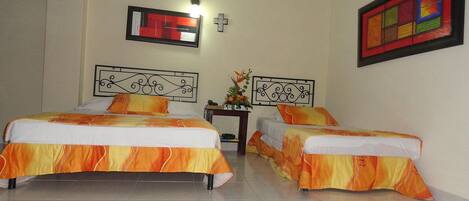 A hotel room with two beds, a small table with a vase of flowers, and a wall-mounted TV.