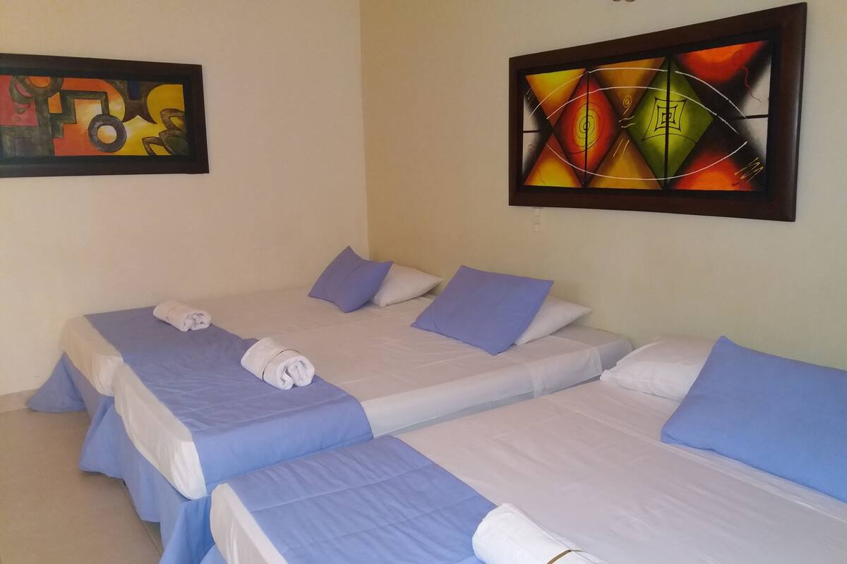 A hotel room with two single beds, each with a blue bedspread and white pillows. There are towels neatly folded on each bed.