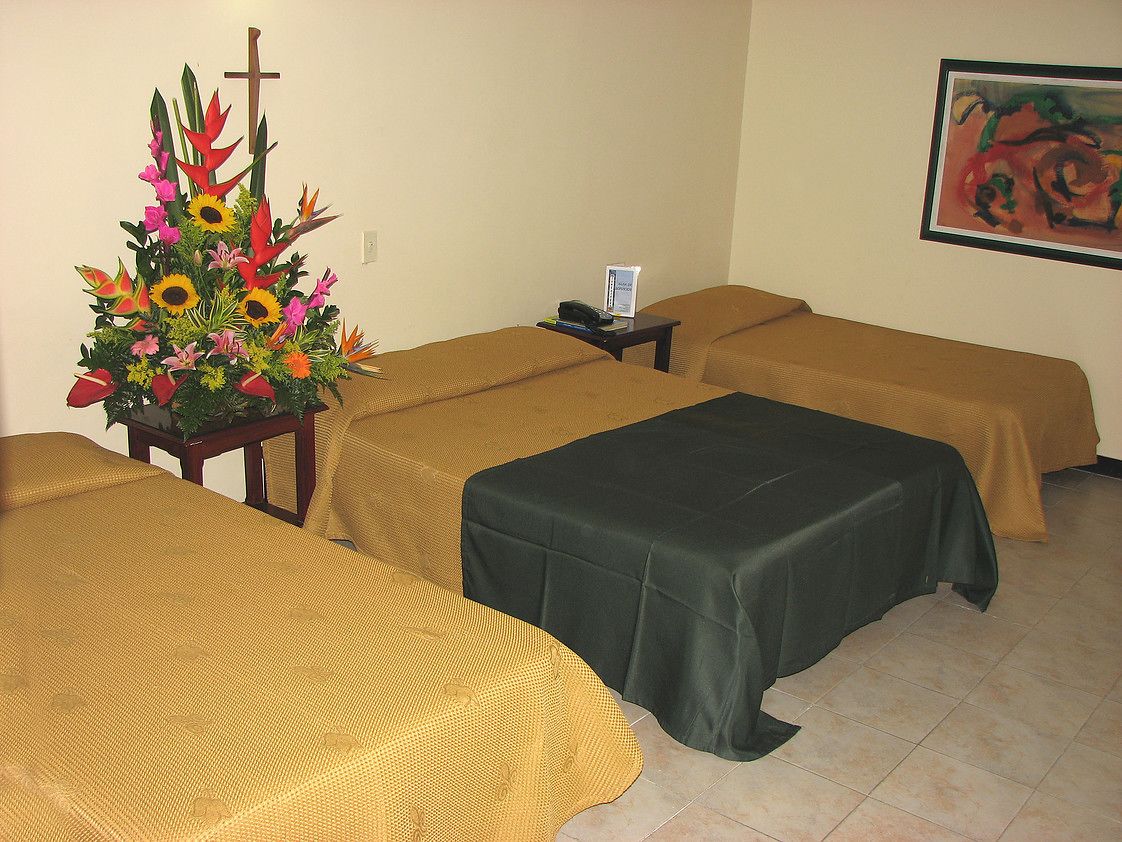 A room with three beds, a small table with a phone, a cross, and a painting on the wall.