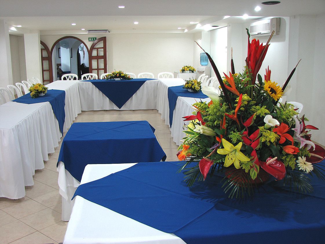 A conference room with tables covered in blue tablecloths, white chairs, and a large floral arrangement.