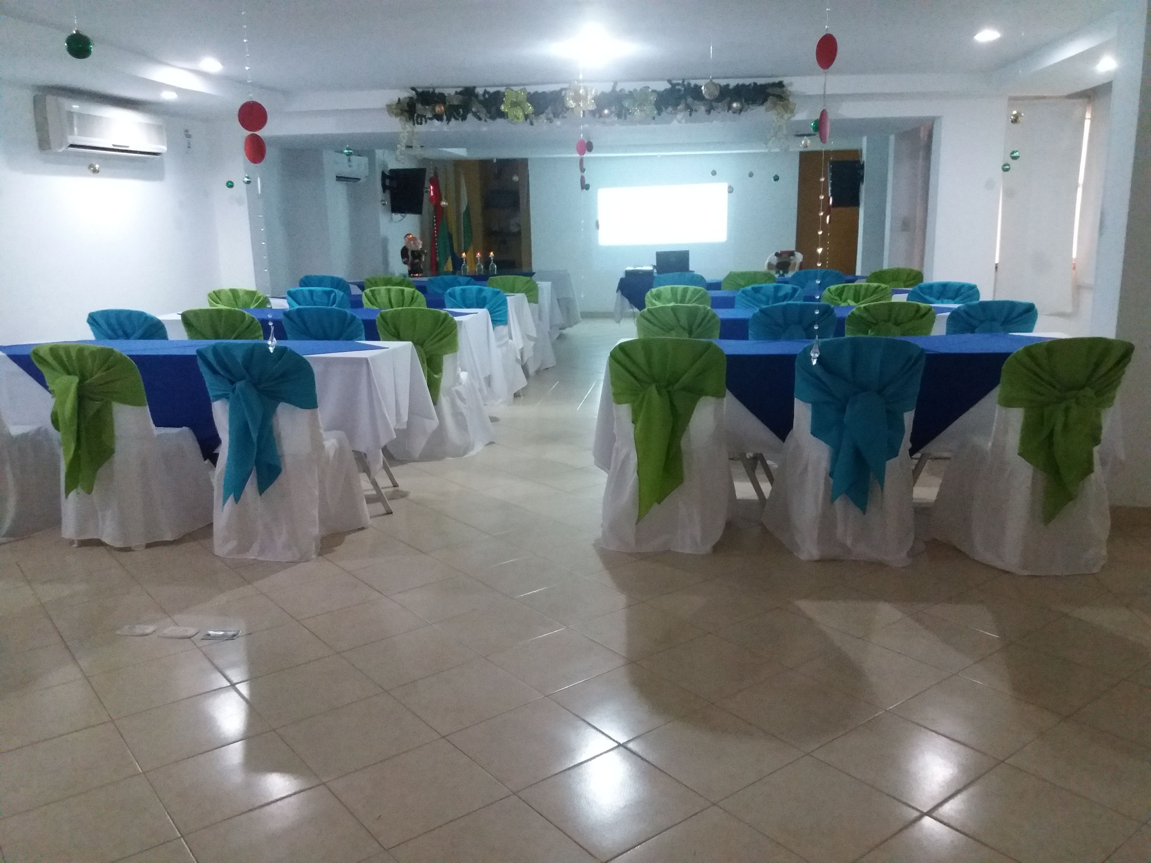 Un salón de conferencias con mesas, sillas, unidades de aire acondicionado y una ventana con cortinas.