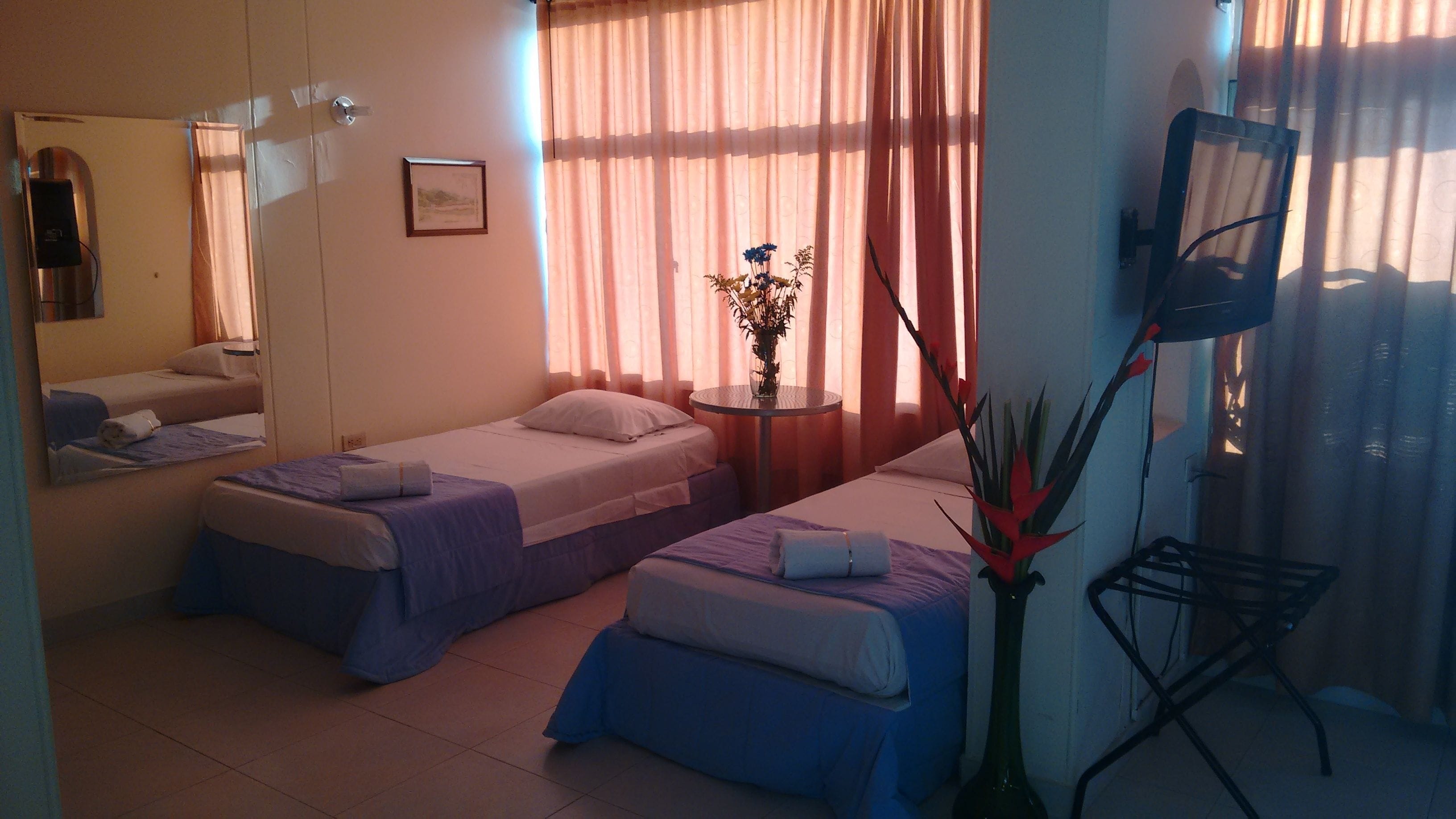 A hotel room with two beds, a round table with a vase, and a mirror on the wall.