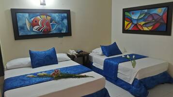 Habitación de hotel con dos camas, cada una con ropa de cama y almohadas azules, una mesita de noche con teléfono, y dos cuadros enmarcados en las paredes.