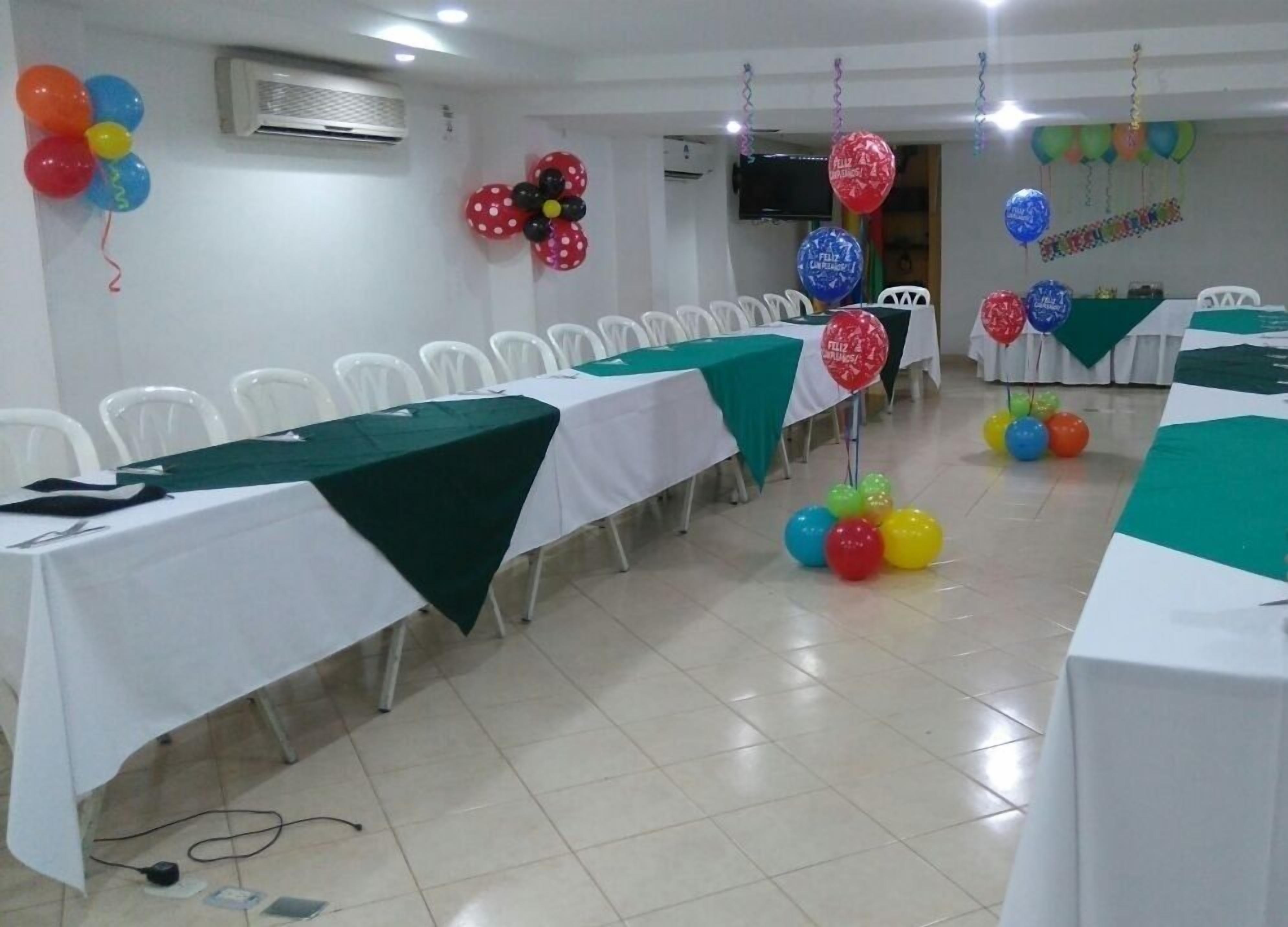 A conference room with rows of white chairs, tables with green tablecloths, and colorful balloons.