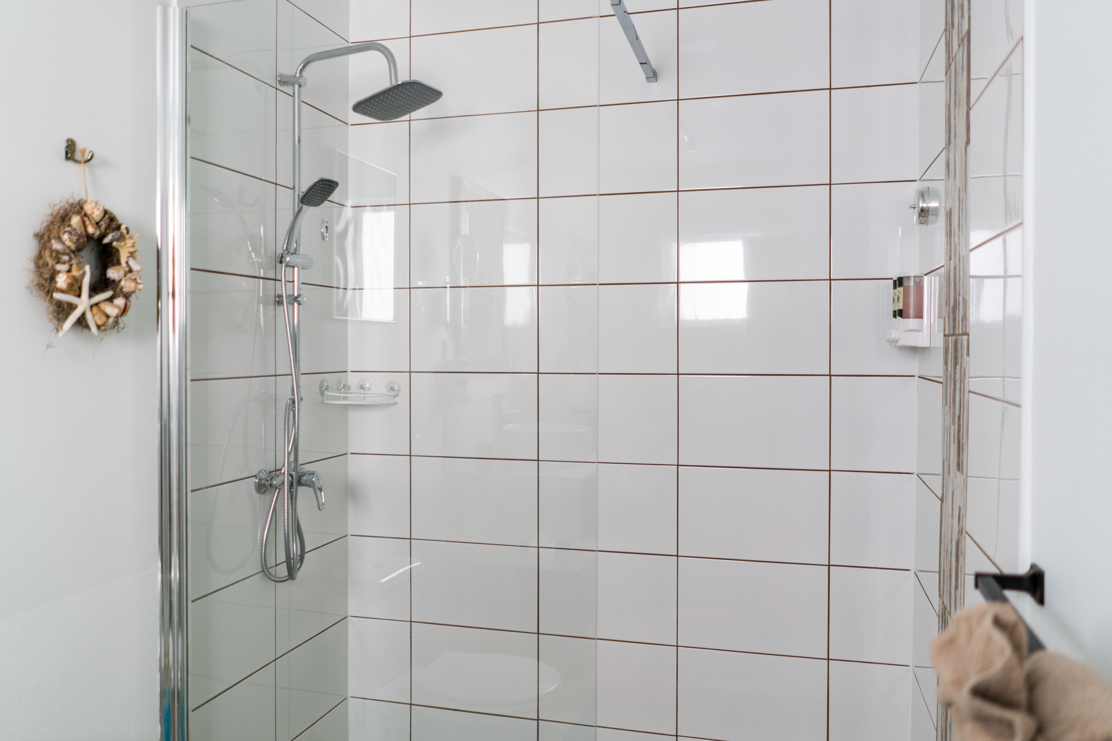 A glass-enclosed shower with a handheld showerhead and a wall-mounted faucet.