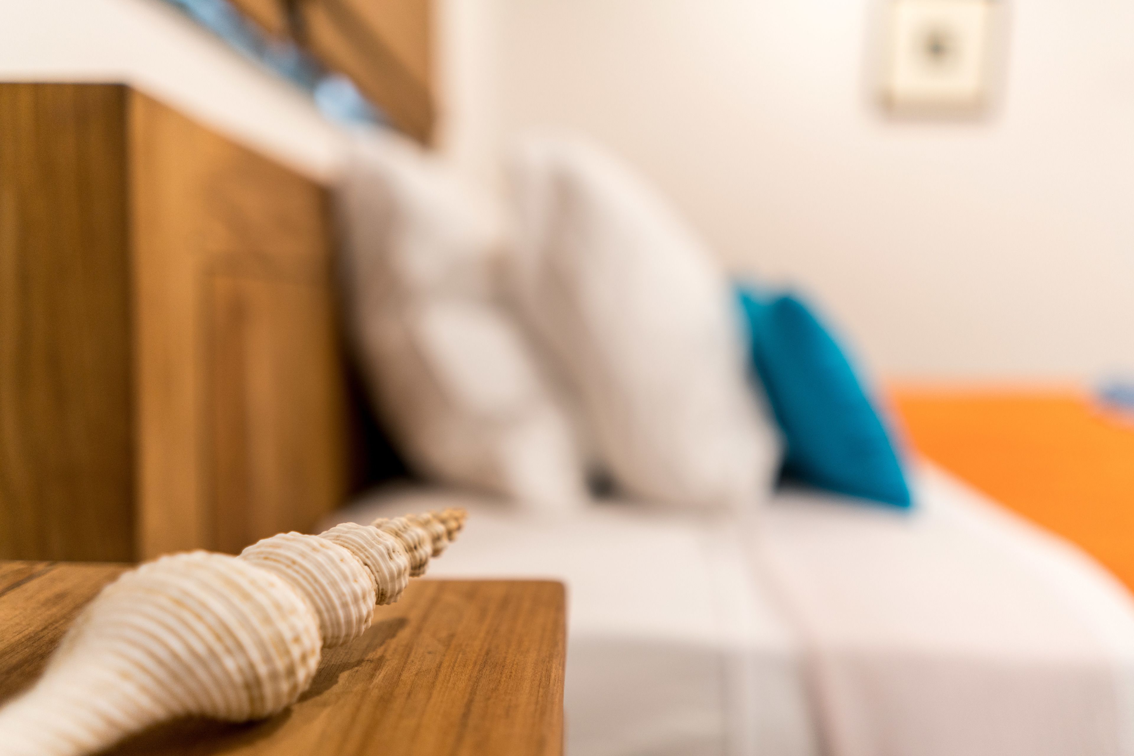 A close-up of a wooden table with a seashell and a white pillow in the background.