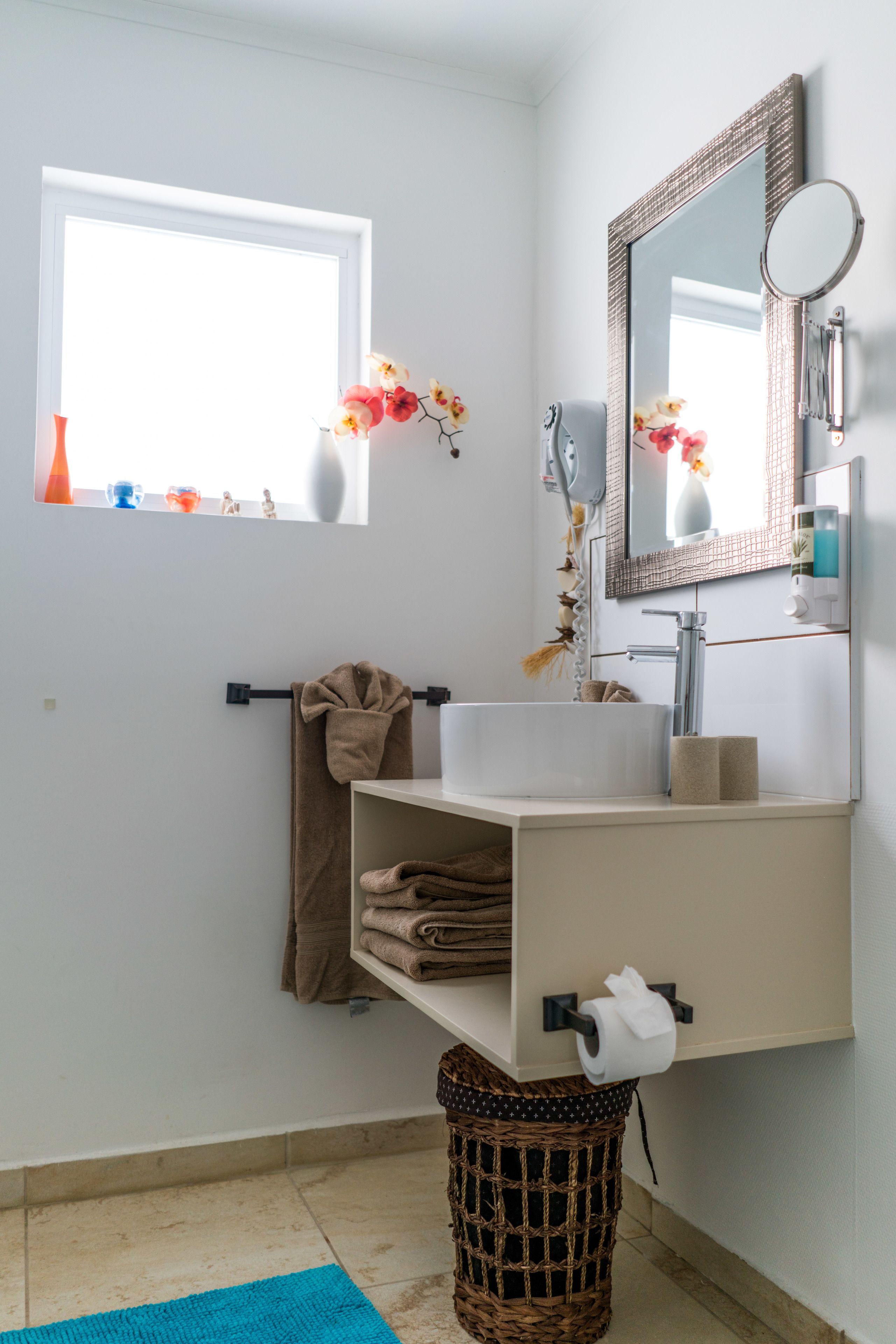 Ein Badezimmer mit einem weißen Waschbecken, einem Spiegel, einem Handtuchhalter und einem Fenster mit Blumen.