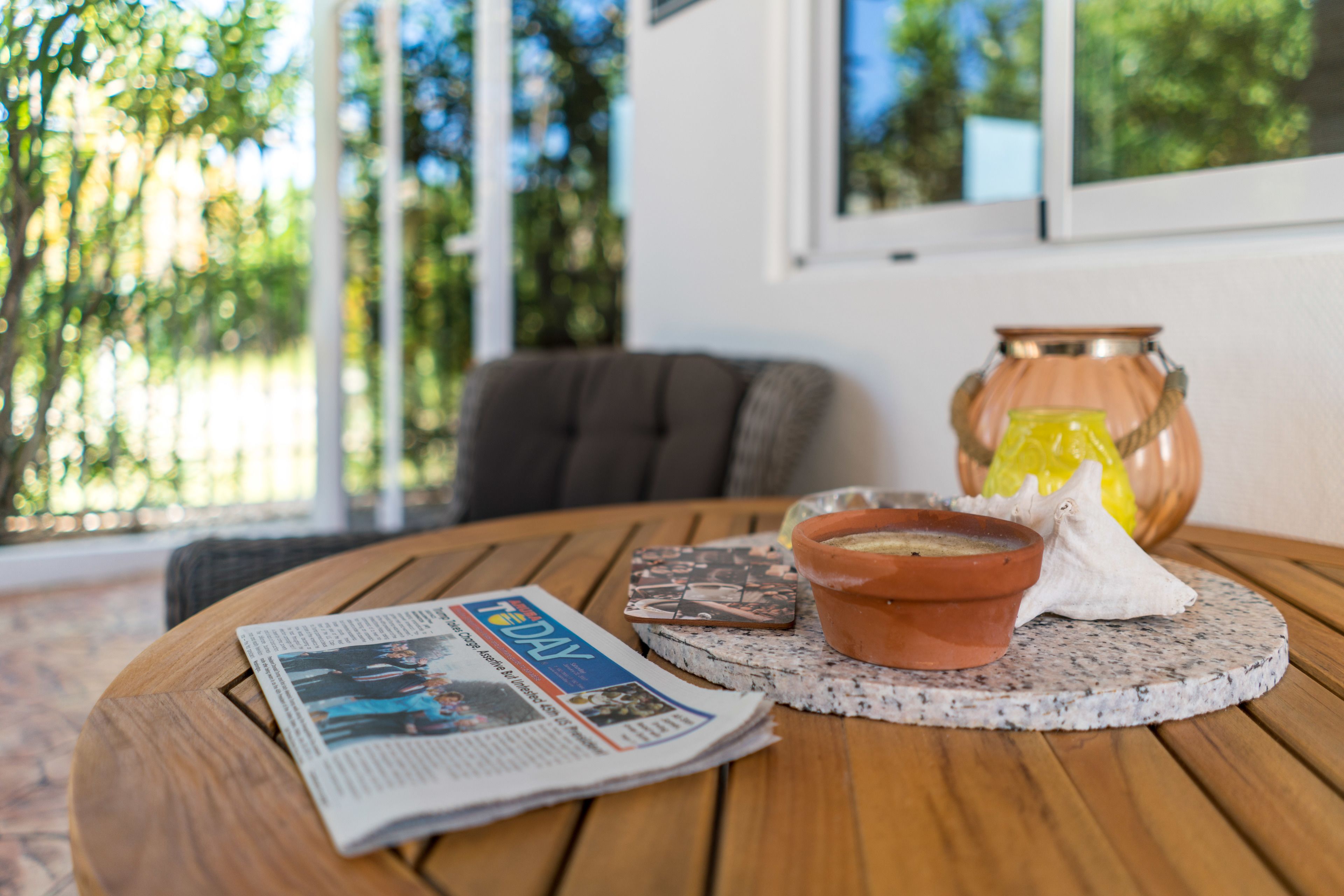 Een ronde houten tafel met een krant, een terracotta schaal en een decoratieve vaas met een citroen.