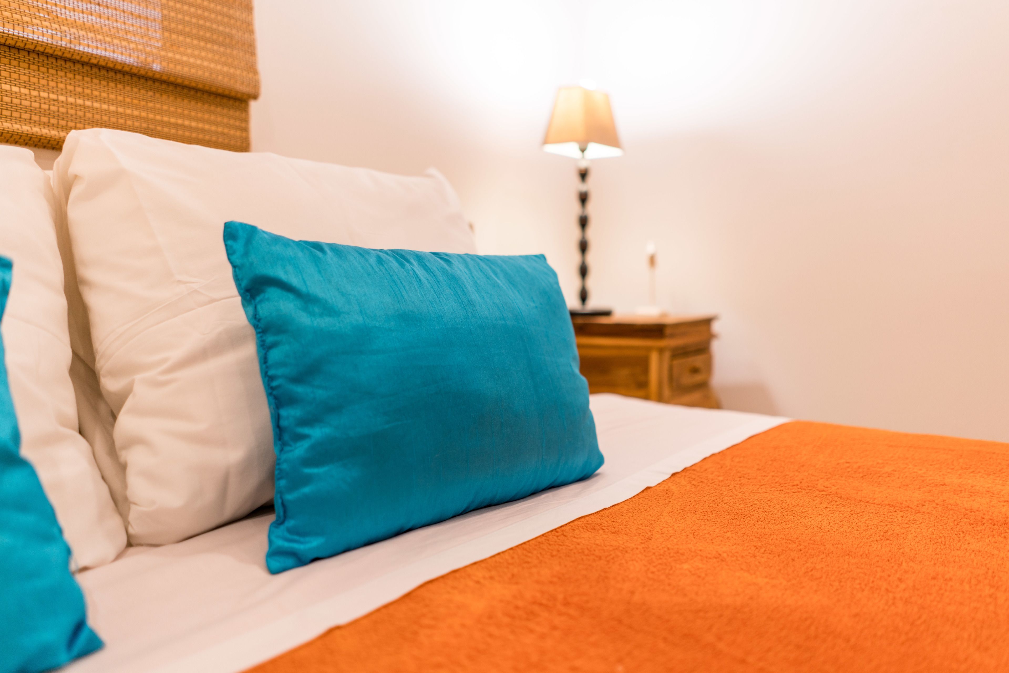 A bed with white and blue pillows, an orange blanket, and a nightstand with a lamp.