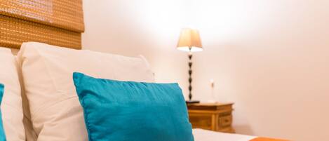 A bed with white and blue pillows, an orange blanket, and a nightstand with a lamp.