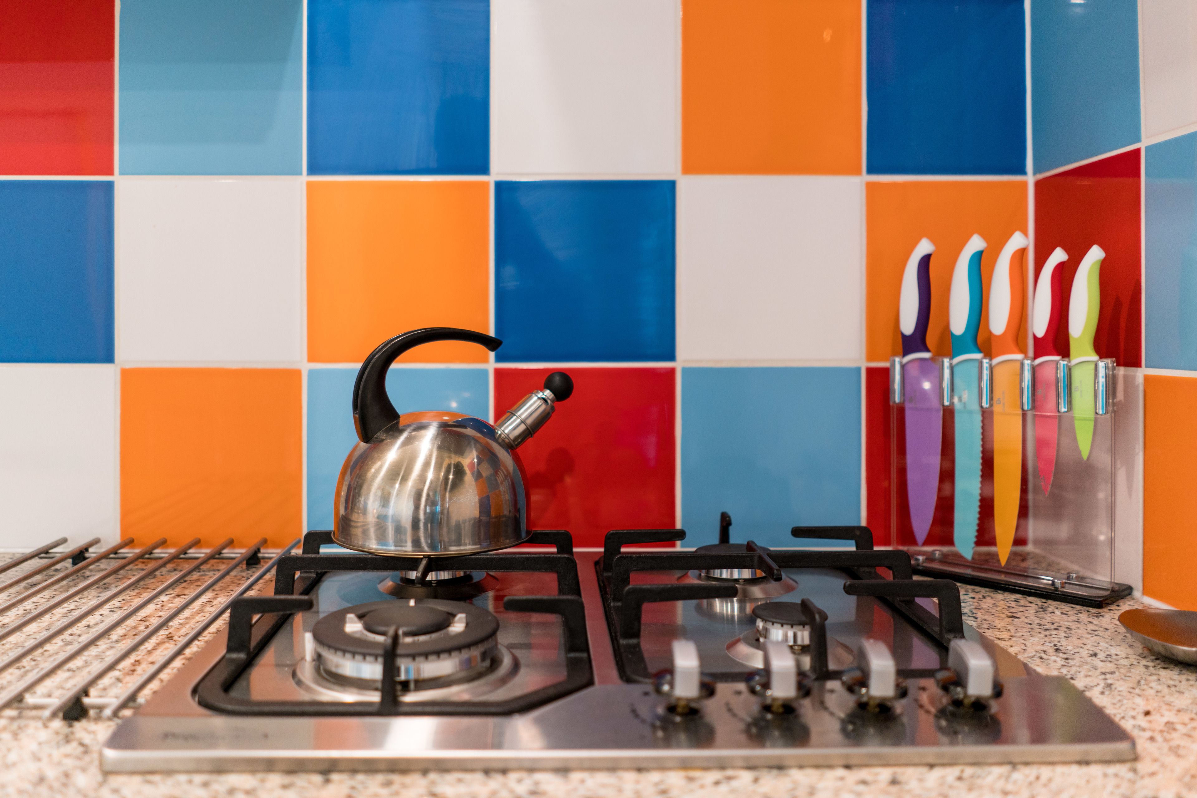 A gas stove with a kettle, a set of knives, and a colorful tiled backsplash.